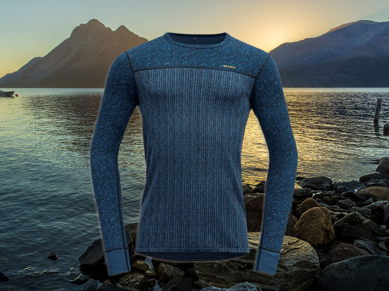 una maglia in lana merino di colore blu in primo piano, sullo sfondo un lago norvegese con le luci del sole di mezzanotte.